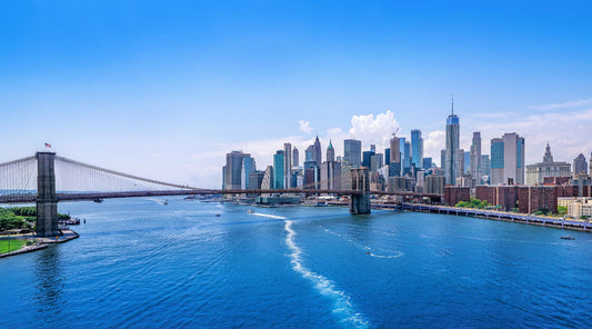 A view of New York City from the river, the sky is bright blue and it's a sunny day.