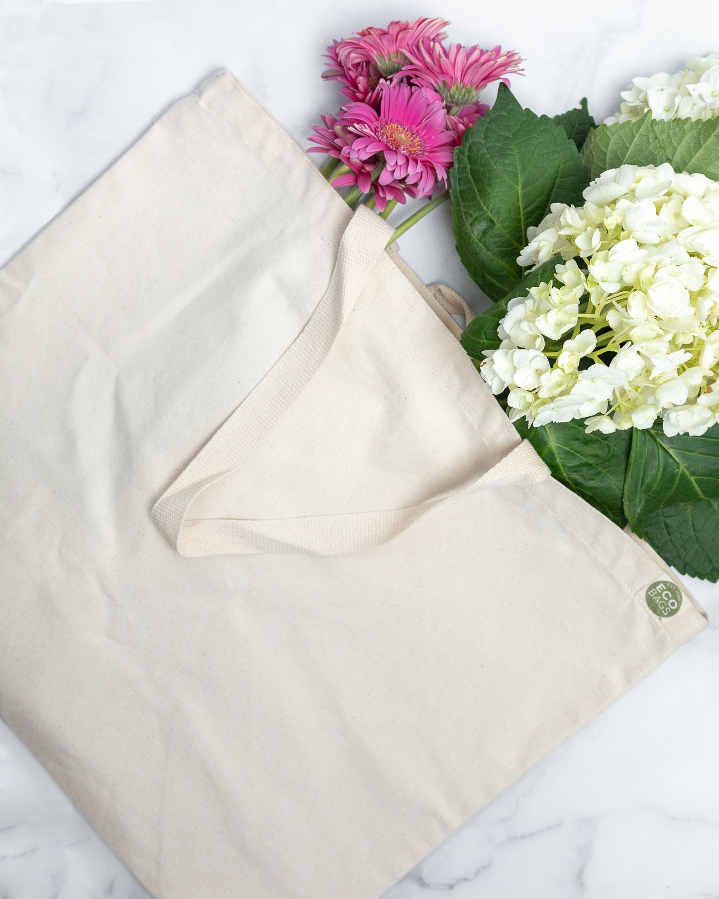 Natural colored large cotton canvas tote bag with pink and white flowers and a visible ECOBAGS green logo