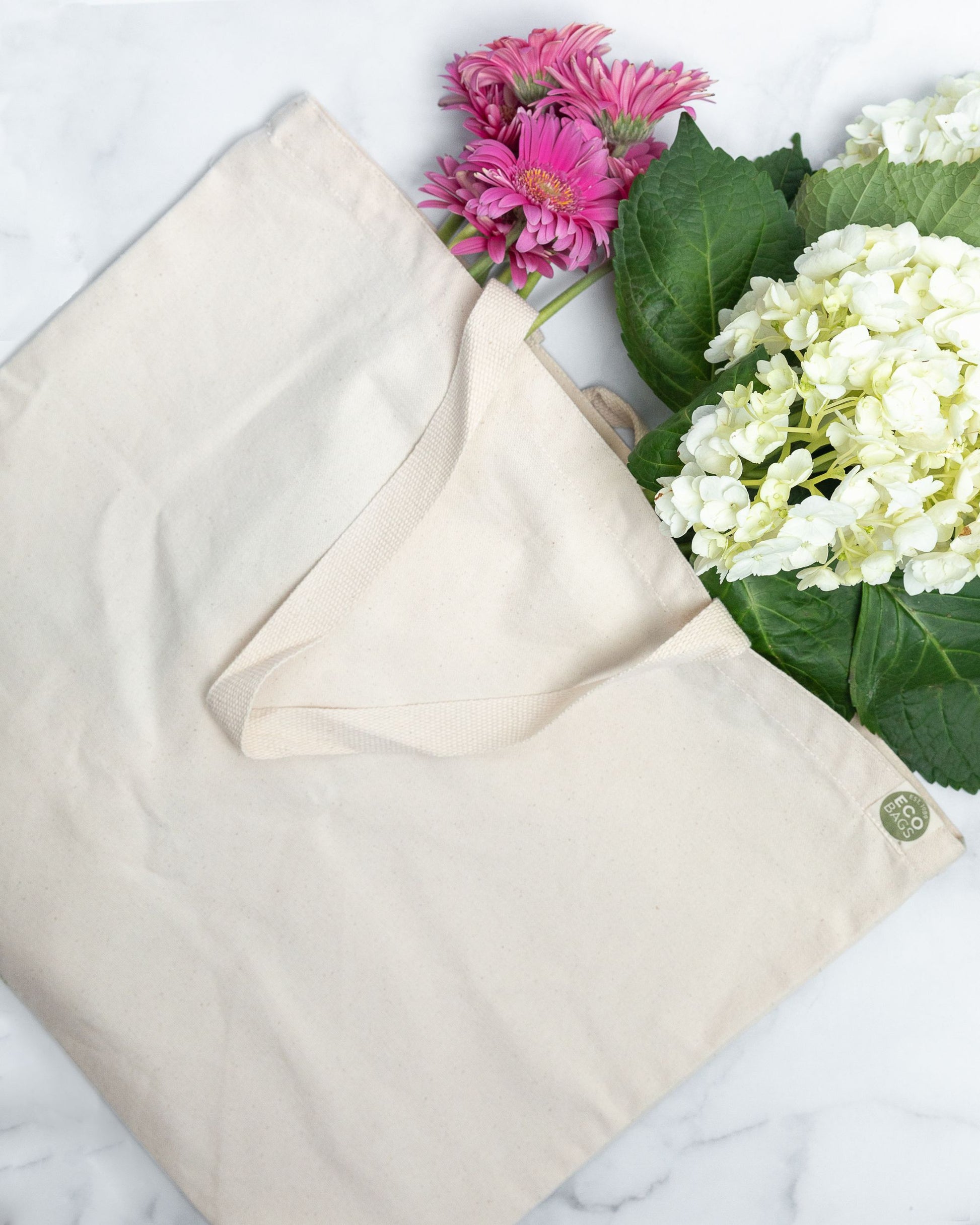 Natural colored large cotton canvas tote bag with pink and white flowers and a visible ECOBAGS green logo