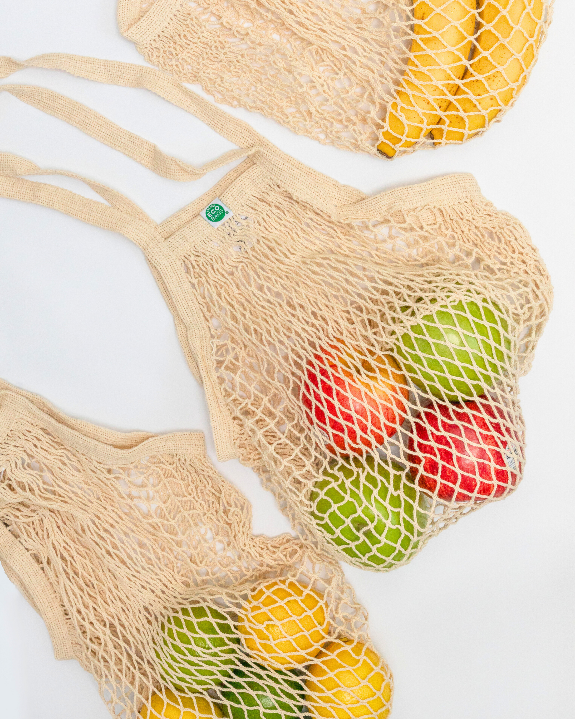 Long handled natural string Mesh produce bags filled with fruits with a visible green ECOBAGS label on a white background