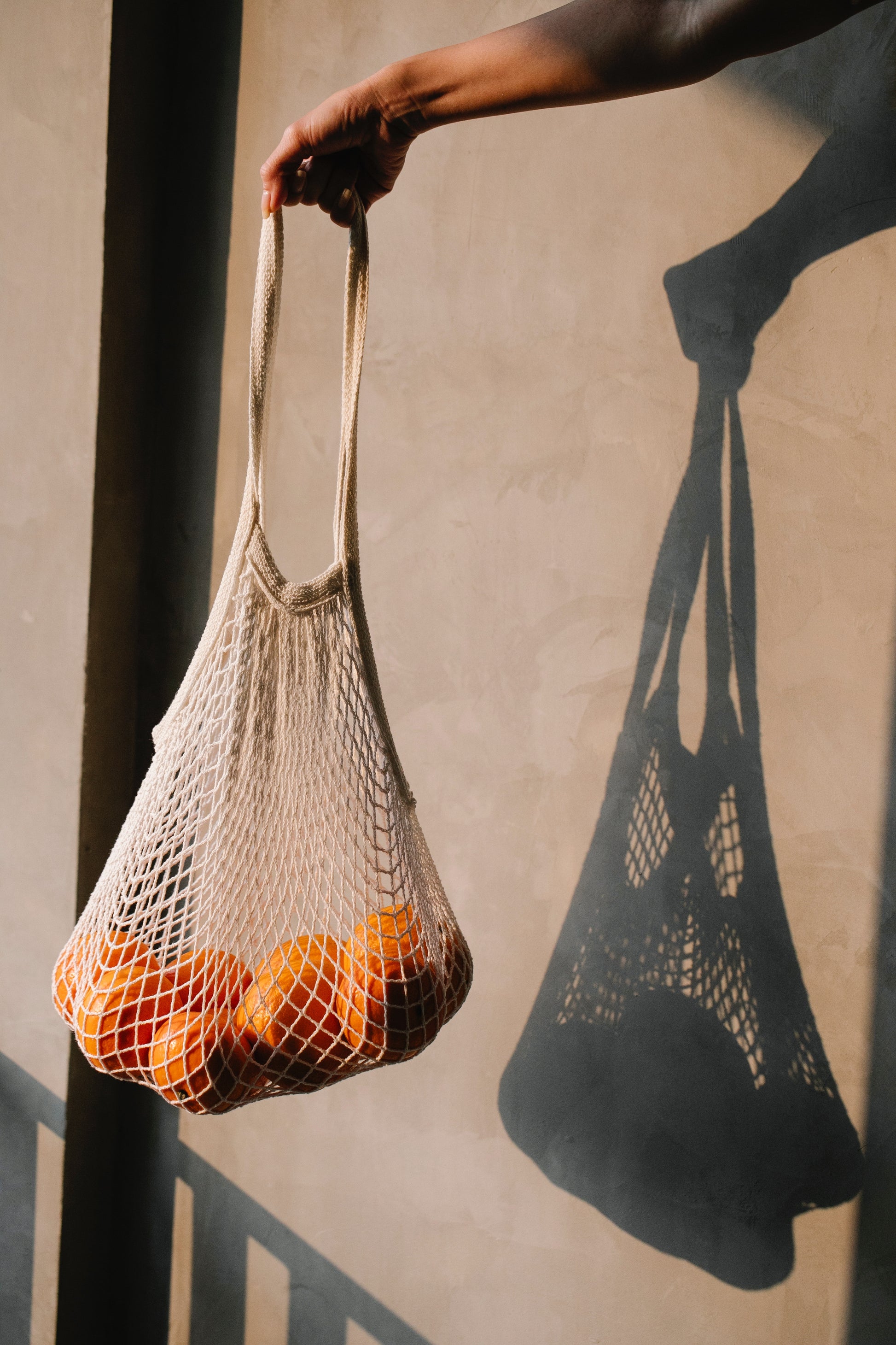 Hand holding a French market  string bag with oranges against a neutral background