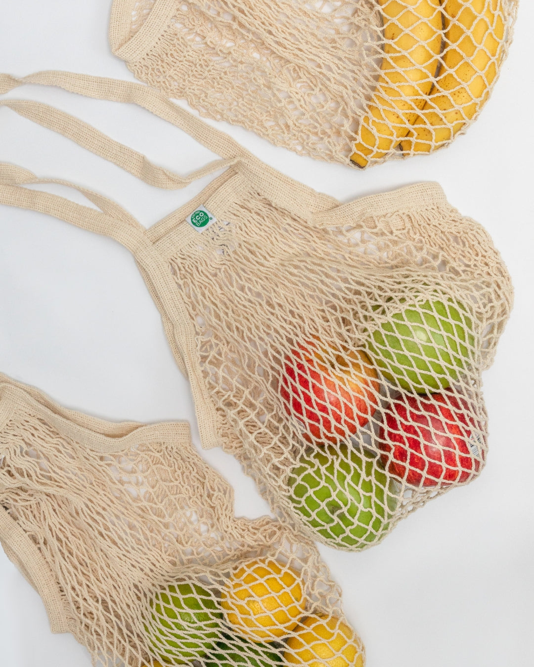 Beige mesh grocery bags filled with fruits on a white background