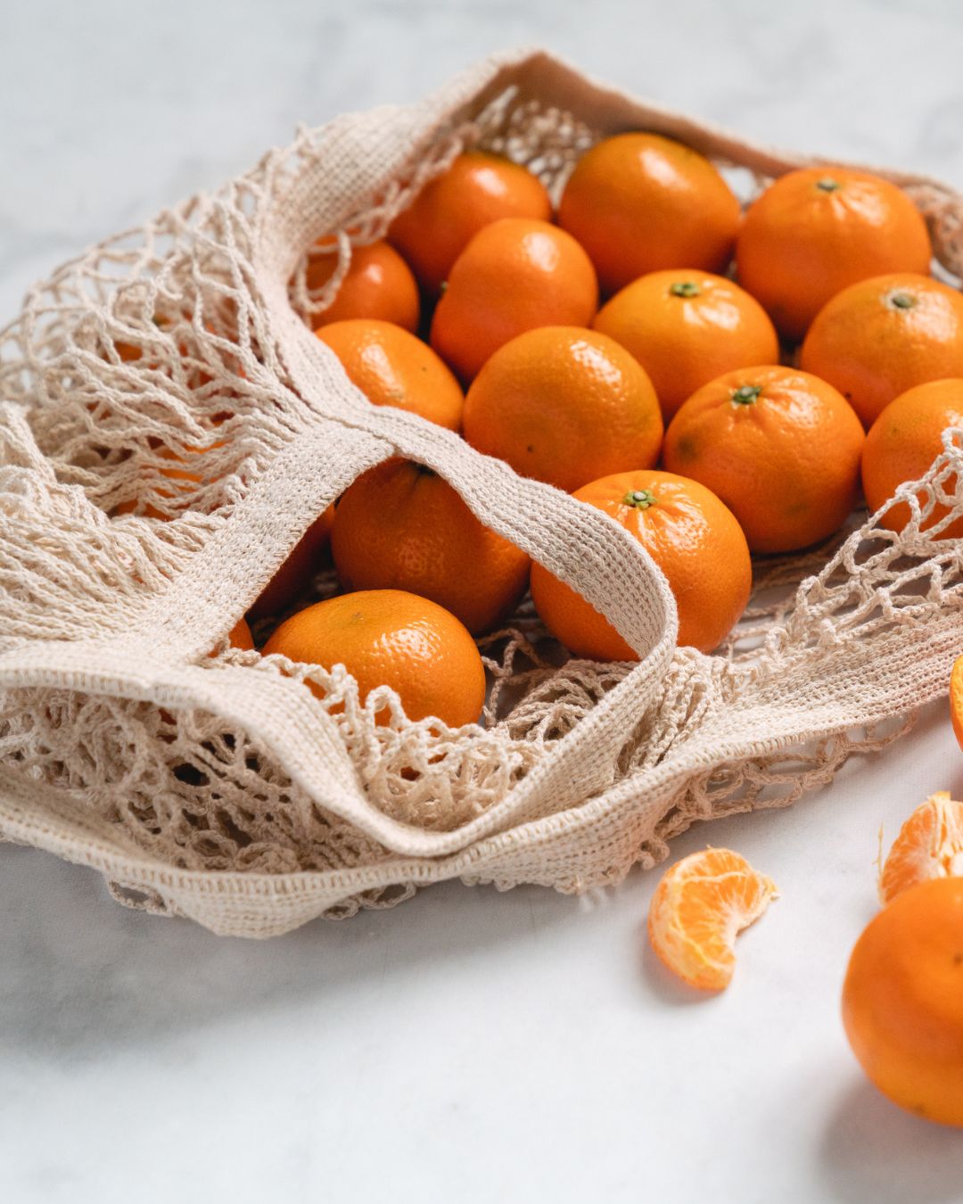 Oranges in a natural undyed cotton net string bag on a light background