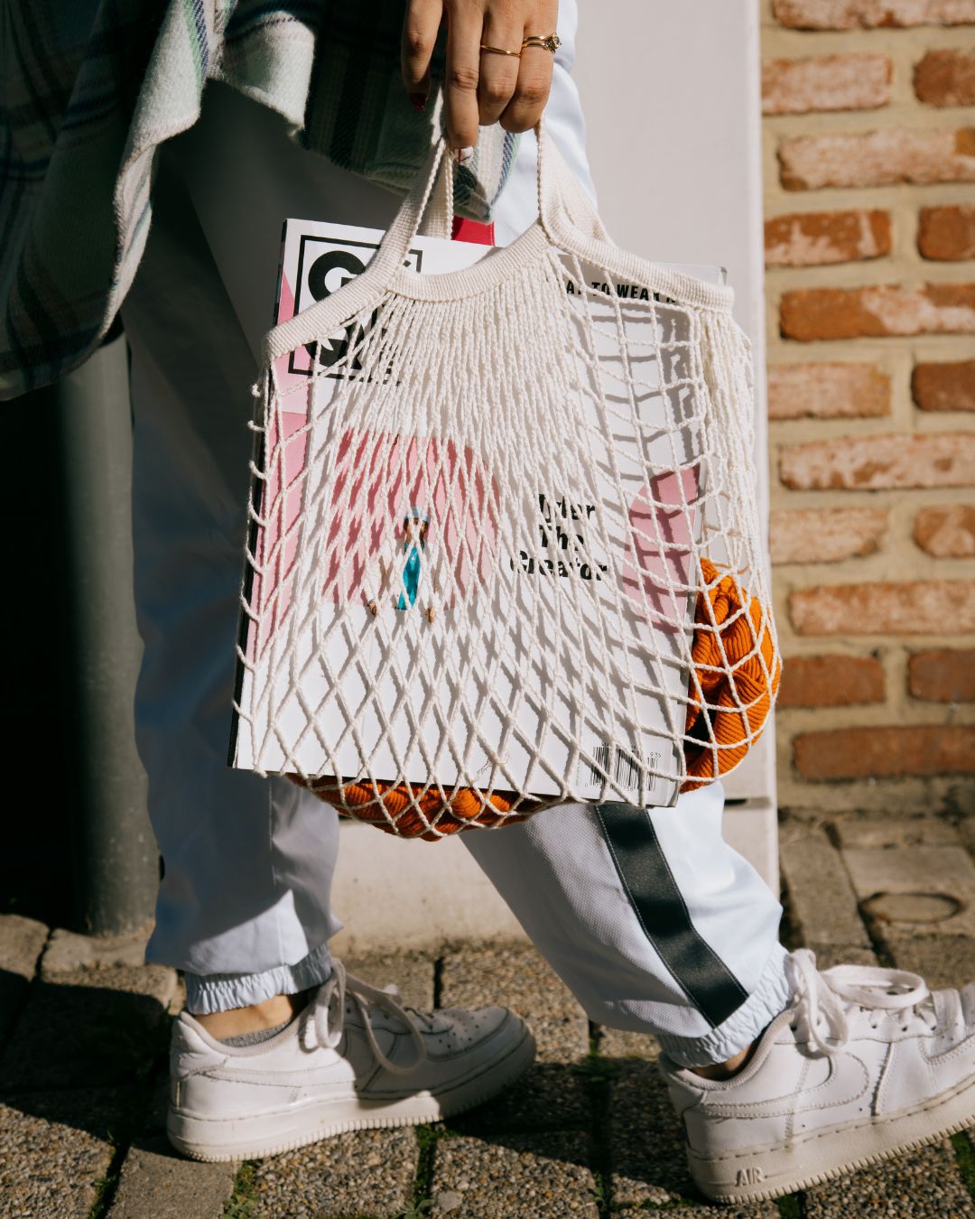 Person holding a net cotton string bag with colorful items against a brick wall.