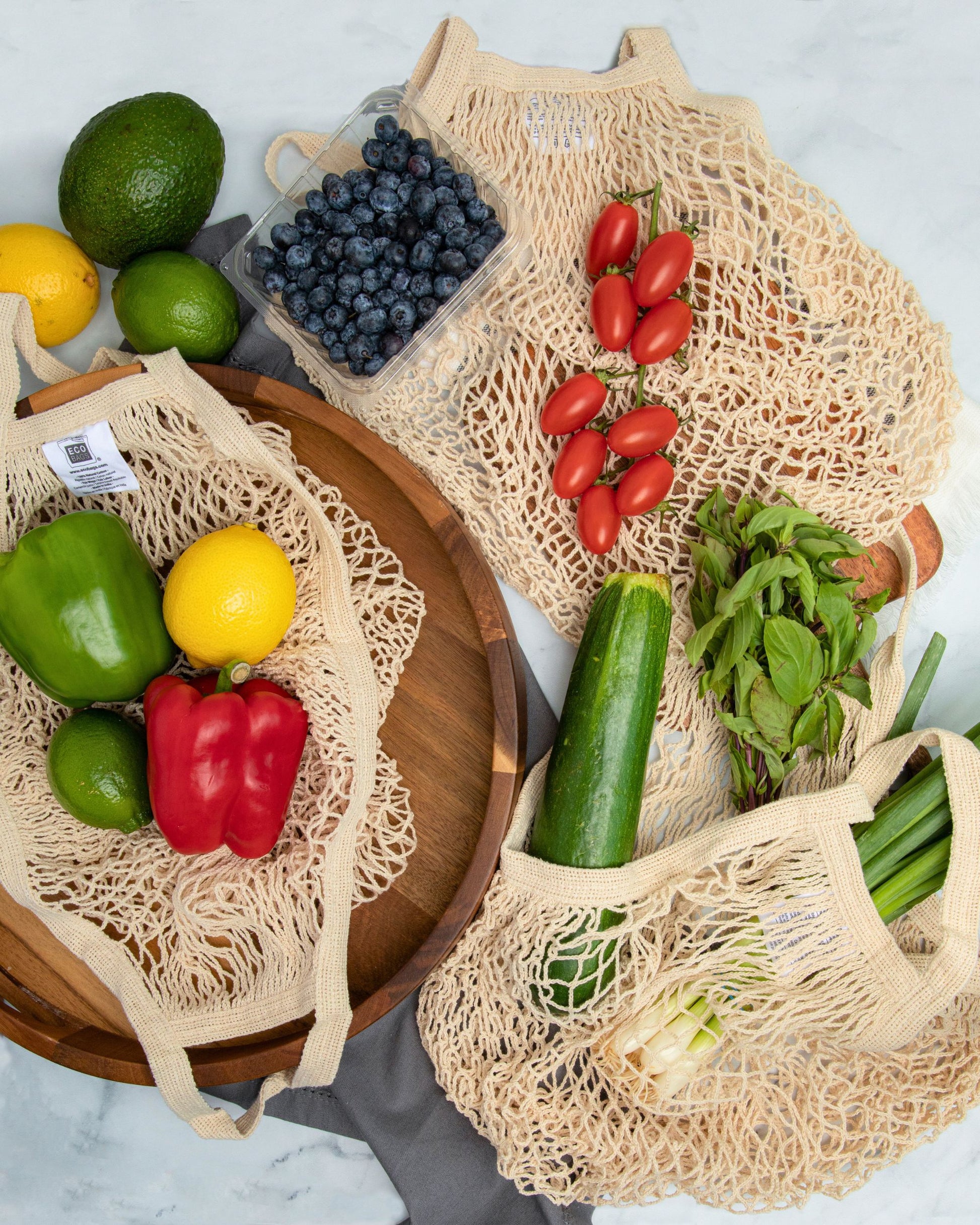 Recycled cotton reusable mesh net string bags filled with bulk produce on a marble surface