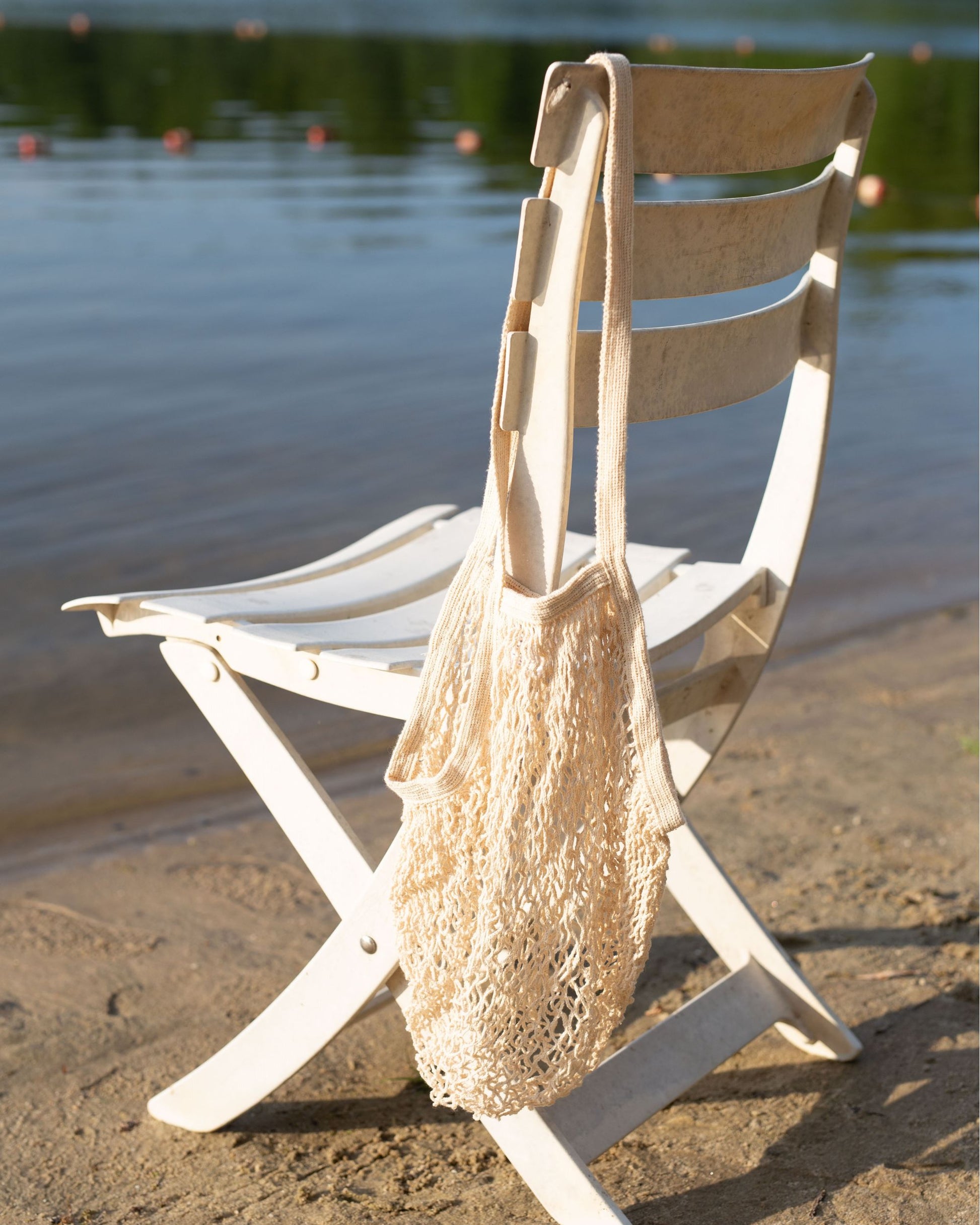 Natural recycled cotton mesh bag on a white folding chair by the water
