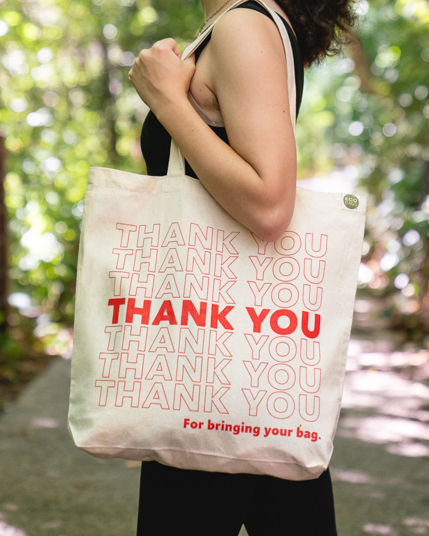Person holding a tote bag with 'THANK YOU' text in red and natural.