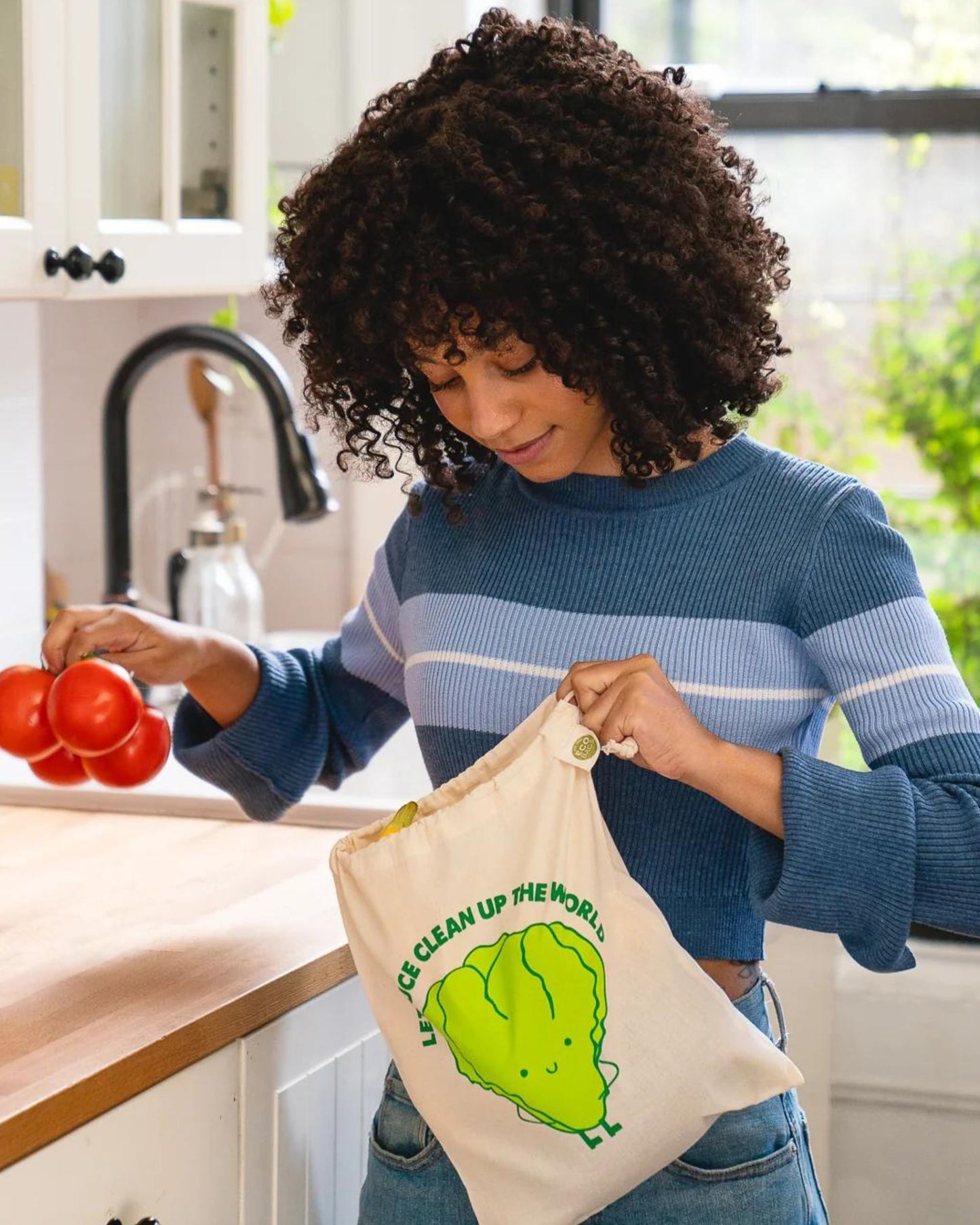 Person in a kitchen holding a reusable produce bag with a green lettuce leaf design.