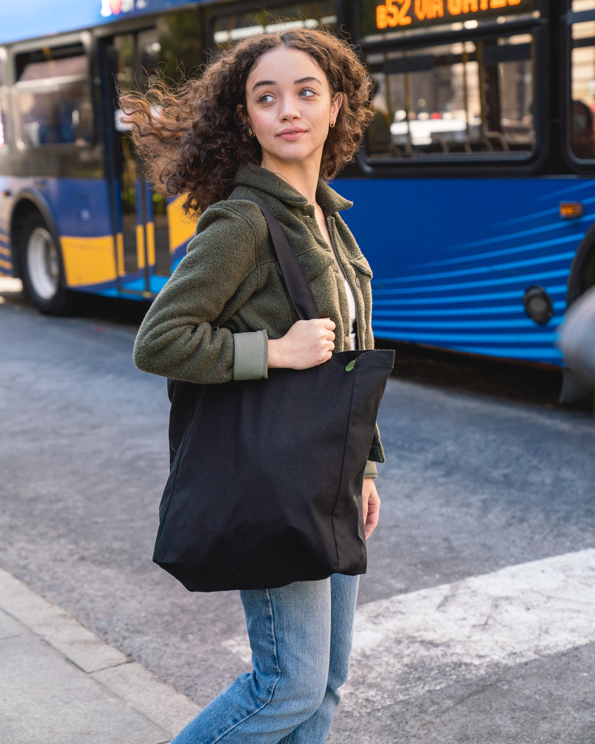 Woman holding a black tote bag on a city street with a bus in the background