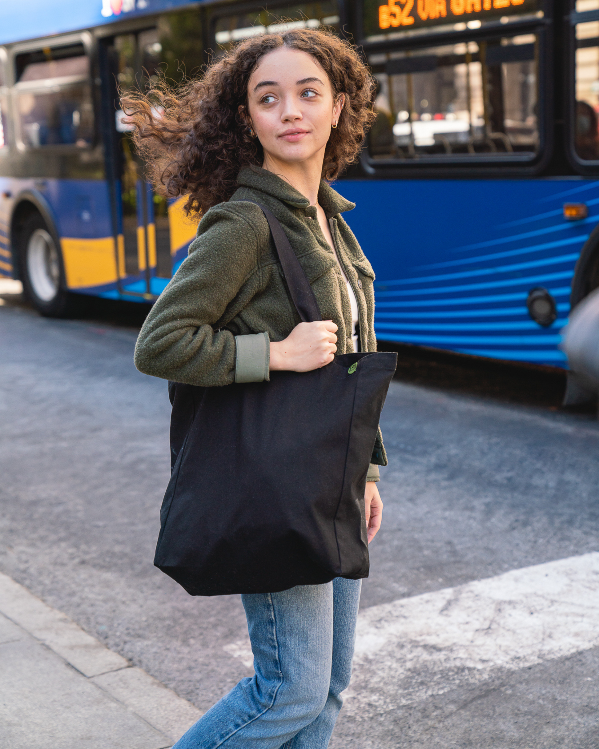 Woman holding a black tote bag on a city street with a bus in the background