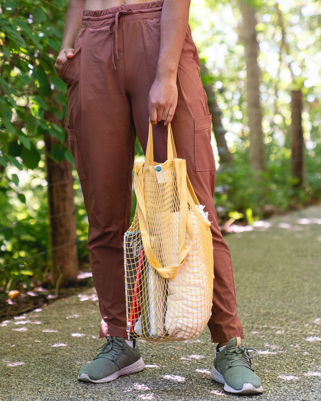 Person holding a yellow reusable string bag with accessories in a forest setting