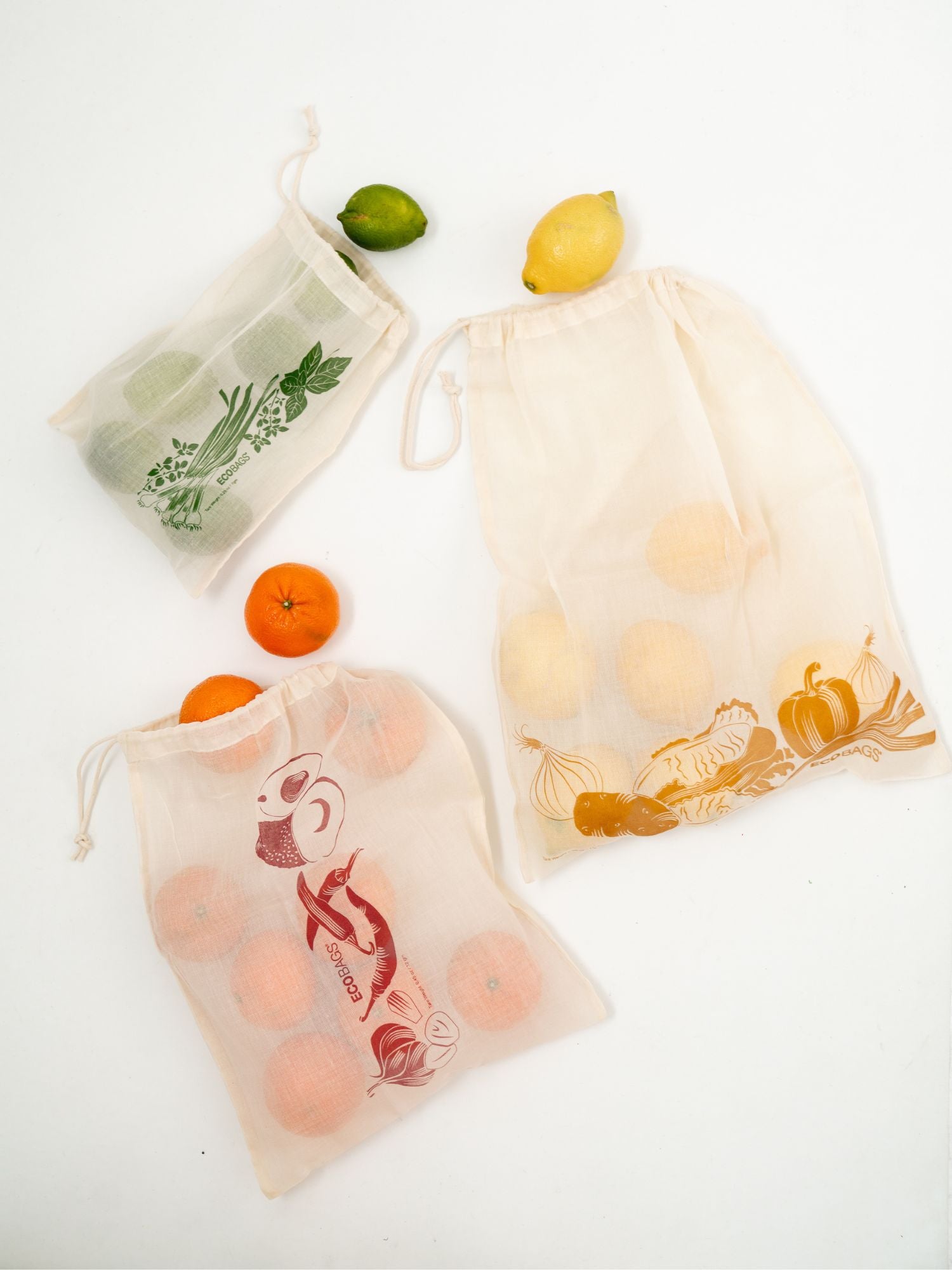 Three organic cotton drawstring bulk bags with fruit and vegetables on a white background